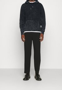 Mikina s kapucí ve vybledlé tmavě modré barvě, vybavená přední kapsou a šňůrkami. Přiřazena k černým zúženým kalhotám a černým botám.