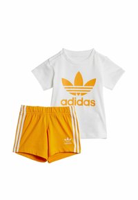 T-shirt en coton blanc avec un grand logo Adidas orange, associé à un short jaune avec des bandes latérales blanches et un petit logo Adidas.