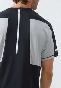 Sportliches T-Shirt mit kurzen Ärmeln, das ein marineblaues und hellgraues Farbblockdesign aufweist. Es hat eine glatte Textur und reflektierende Akzente auf der Rückseite.