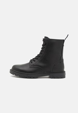 Bottines en cuir noir avec un laçage, bout arrondi et semelle texturée. Dotées d'une languette et de détails minimalistes sur le talon.