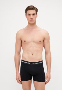 Schwarze Boxer-Shorts mit einem weißen Gummibund, auf dem "JACK & JONES" steht. Hergestellt aus glattem, dehnbarem Stoff, im taillierten Design.