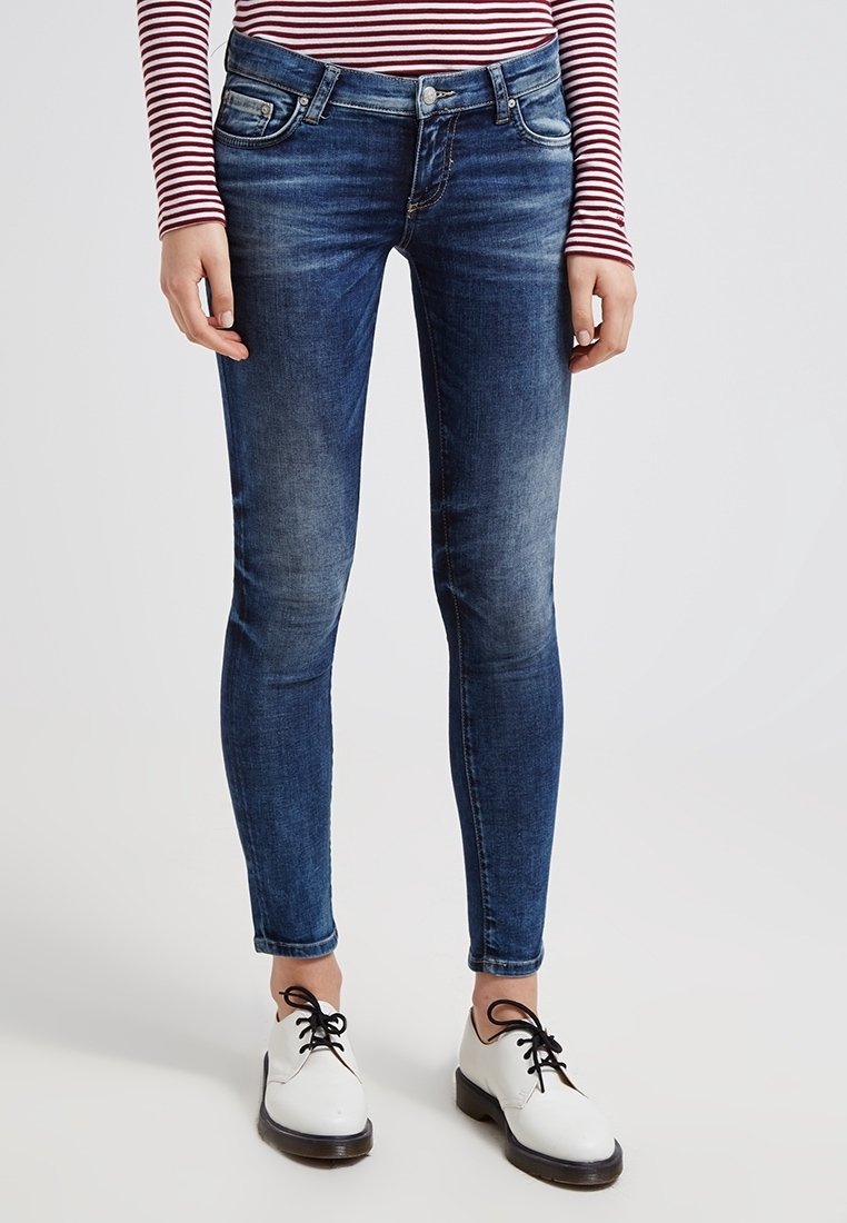 Jeans skinny de color azul con un lavado desgastado, que cuentan con cinco bolsillos, trabillas para el cinturón y un cierre con cremallera. Combinados con zapatos blancos de cordones.