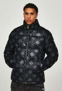 Black puffer jacket featuring a quilted design with embossed patterns. High collar, front zip closure, and side pockets with zipper details.