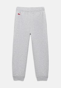 Calças de treino cinza claro com cintura e punhos elásticos, pequeno logotipo de crocodilo vermelho no quadril esquerdo, exibidas sobre fundo branco.