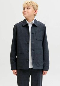 Tamsiai mėlynas languotas švarkas su apykakle, priekyje užsegamas sagomis, dvi priekinės kišenės ir lygus, tekstūruotas audinys. Derinamas su po apačia esančia balta palaidine.