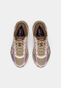 Καφέ και μπεζ αθλητικά παπούτσια με υφή από δίχτυ, κλείσιμο με κορδόνια, μοβ λεπτομέρειες και μαλακή σόλα, με το λογότυπο της ASICS στη γλώσσα.