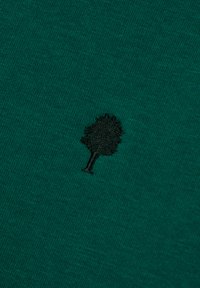 Teal stof met een kleine zwart geborduurde boom-symbool in het midden van het oppervlak.