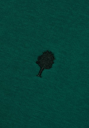 Teal stof met een kleine zwart geborduurde boom-symbool in het midden van het oppervlak.