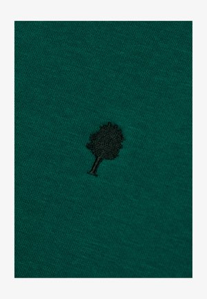 Teal fabric with a small black embroidered tree symbol centered on the surface.