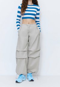 Gestreepte blauw-witte cropped trui, beige wijde broeken met zakken, en lichtblauwe sneakers met grijze accenten.