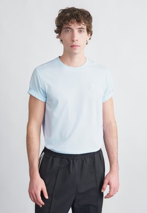 T-shirt di cotone azzurro con maniche arrotolate, con un piccolo logo bianco sul petto, abbinata a pantaloni scuri con vita elastica.