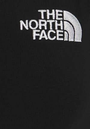 Logo blanc brodé "THE NORTH FACE" avec un design en quart de cercle sur un fond de tissu noir.