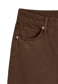 Brązowa tkanina dżinsowa z wygiętym paskiem, przednia kieszeń z subtelnym przeszyciem oraz metalowy guzik na pasku.