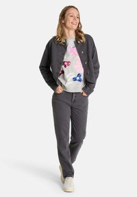 Grau denimjacke mit Knöpfen, grauer sweatshirt mit bunten, glitzernden Blumenmustern und passenden grauen Hosen mit weißen Sneakers.
