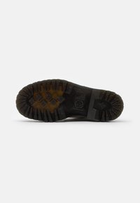 Suela de bota de goma negra con un diseño de profunda banda de rodadura, que presenta patrones circulares y triangulares para una mejor tracción y durabilidad.