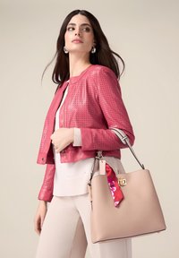 Giacca in pelle perforata rosa con colletto arrotondato, abbinata a una borsa leggera beige con una tracolla decorata con fiori.