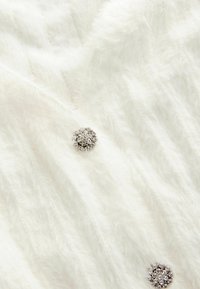 Vit pälstof med en mjuk textur, prydd med cirkulära dekorationer med flera glittrande stenar som accenter.