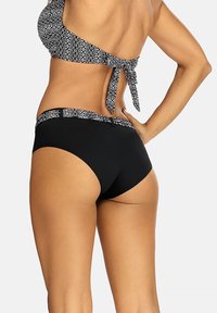 Czarne majtki bikini z wzorzystym pasem. Góra ma krój na jedno ramię, związana z tyłu, prezentując gładką fakturę.