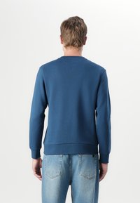 Felpa blu navy con maniche lunghe, scollo tondo e polsini a costine; abbinata a jeans di denim azzurro con tasche posteriori.