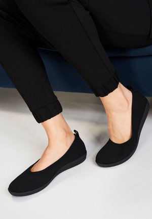 Sorte slip-on sko med en tekstureret strikket overdel og rund tå. Har en lav kilehælssål og en træktab ved hælen for nem påtagning.