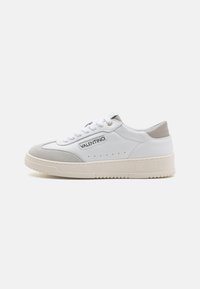 White leather sneaker with grey suede accents, round toe, lace-up design, perforated details on the sides, and a textured rubber sole.