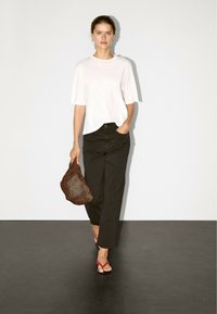 Light pink short-sleeve t-shirt, black wide-leg pants, brown netted bag, and pink thong sandals. Smooth fabric and relaxed fit.