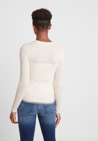 Jersey de manga larga color crema con patrón de espiga texturizado en la parte superior de la espalda, cuerpo acanalado y ribete en contraste en el dobladillo y los puños.