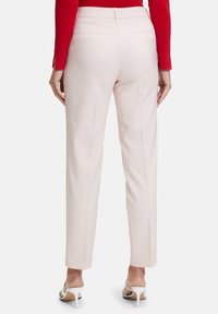 Pantaloni su misura rosa chiaro con una vestibilità slim, dotati di due tasche posteriori e una superficie liscia, abbinati a sandali bianchi con tacco alto.
