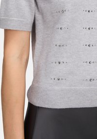 Szary sweter z dzianiny z krótkim rękawem, zdobiony poziomymi rzędami dekoracyjnych ćwieków. Prążkowany dół i mankiety, miękka tekstura oraz dopasowany krój.