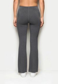 Szare dzwonowate legginsy wykonane z miękkiej, elastycznej tkaniny, charakteryzujące się gładką teksturą i wysokim stanem. W połączeniu z białymi trampkami.