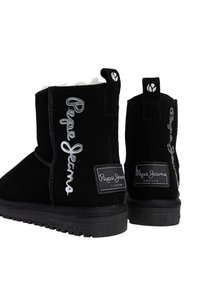 Juodi zomšiniai kulkšninių botai su balta pūkuota pamušalu. Yra iškilnių ženklų ir juodas guminis padas. Dizainą papildo šoninis akcentas.