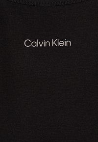 Crna pamučna majica s okruglim izrezom. Na prednjoj strani se nalazi logo "Calvin Klein" u bijeloj boji, centriran, u sans-serif fontu. Mekana tekstura, kroj koji se prilagođava tijelu.