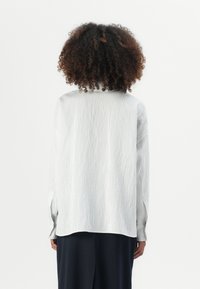 Leicht gestreiftes Langarmshirt aus weichem Stoff mit einer lockeren Passform, verfügt über einen abgerundeten Saum und knöpfbare Manschetten, von hinten gezeigt.
