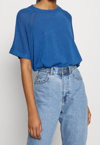 Modré oversized pletené tričko s krátkými rukávy a texturovaným povrchem, zkombinované s vysokým pasem světlými modrými džínami.