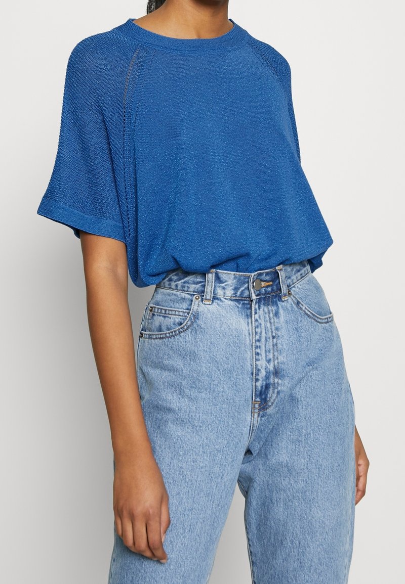 Modré oversized pletené tričko s krátkými rukávy a texturovaným povrchem, zkombinované s vysokým pasem světlými modrými džínami.