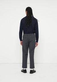 Granatowy sweter z dzianiny i szare spodnie o luźnym kroju, z bocznymi kieszeniami i elastycznym paskiem; w zestawie z czarnymi butami i białymi skarpetkami.