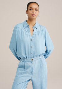 Hellblaues, lässig geschnittenes Denim-Hemd mit langen Ärmeln, Knopfleiste und Kragen. Mit Falten an den Schultern und einer glatten Textur.