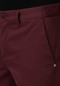 Burgundowe spodnie z fakturowanej tkaniny, z zapięciem na guzik i bocznymi kieszeniami. Wyraźny akcent z logo przy kieszeni.