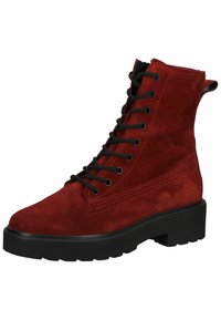 Bottine en daim rouge à lacets noirs, avec une semelle en caoutchouc robuste et des détails de coutures renforcées sur les côtés. Forme de bout structurée et arrondie.
