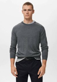 Grå långärmad tröja med rund halsringning i ett glatt tyg, lagd över en ljusgrå skjorta, kombinerad med mörka byxor och ett vävt bälte.