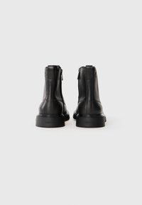Botas de tobillo de cuero negro con un acabado texturizado, que cuentan con un cierre de cremallera y una suela de goma gruesa. Marca Calvin Klein en la suela.