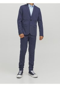 Granatowy garnitur z jednorzędową marynarką z jednym guzikiem, dwoma przednimi kieszeniami, połączony z jasnoniebieską koszulą i ciemnymi sneakersami. Slim-fit design.