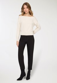 Maglione lavorato a maglia color crema con scollo a barca abbinato a pantaloni neri sartoriali e stivaletti neri con tacco. Tessuto morbido, design aderente, stile minimalista.