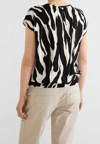 Schwarze und weiße kurzärmelige Bluse mit einem Zebra-Streifen-Muster, locker geschnitten und mit elastischem Bund, kombiniert mit beigen Hosen.