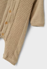 Cárdigan de punto beige con un patrón texturizado, puños acanalados y botones de madera en la parte delantera. Tejido suave de peso medio.