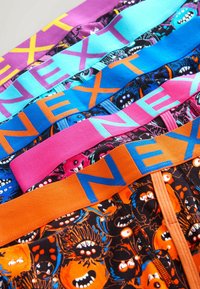 Cuatro pares de calzoncillos de colores para hombre con cinturas estampadas. Los colores incluyen púrpura, turquesa, rosa y naranja, con diseños de monstruos.
