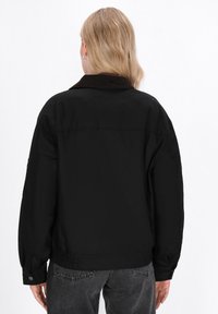 Zwarte bomberjack met een corduroy kraag, elastische manchetten en zoom. Heeft een gladde stoftextuur, met een comfortabele pasvorm en een minimalistisch ontwerp.