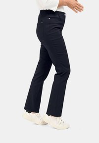 Zwarte broek met een slim fit, elastische tailleband en voorzakken, gecombineerd met witte sneakers. De stof heeft een soepele textuur en minimale stiksels.