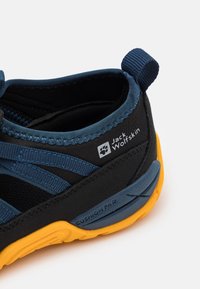 Black and blue athletic shoe with a textured upper, yellow outsole, elastic straps, and a heel loop. Features "CUSHION PAD" label.