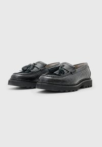 Schwarze Leder-Loafer mit Quasten, ausgestattet mit einer strukturierten Oberseite, dicken Gummisohlen und dekorativen Nähten entlang der Ränder.